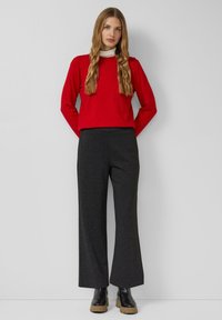 Roter Pullover mit langen Ärmeln aus weichem Stoff, kombiniert mit weiten, dunkelgrauen Hosen und schwarzen Stiefeletten mit dicker Sohle.