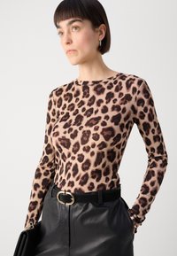 Langermet, tettsittende topp med leopardmønster i brune nyanser på en beige bakgrunn, kombinert med høyt liv, svarte skinnbukser og et svart belte.