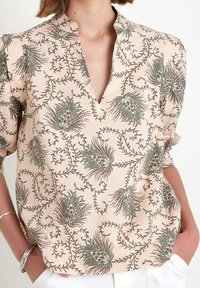 Hedvábná blůza s květinovým vzorem v jemné broskvové barvě. Má výstřih do V, krátké rukávy, komplikované zelené a červené květinové vzory a uvolněný střih.