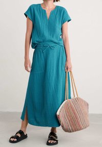 Teal, teksturoitu kahden osan asu, johon kuuluu lyhythihainen paita ja maksihame, jossa on sivuaukko, yhdistettynä moniväriseen kudottuun laukkuun.