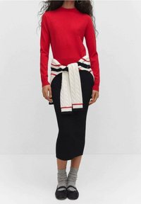 Pull rouge en tricot, jupe midi noire, pull crème en tricot torsadé noué à la taille avec des rayures rouges et noires, chaussettes grises et ballerines noires.