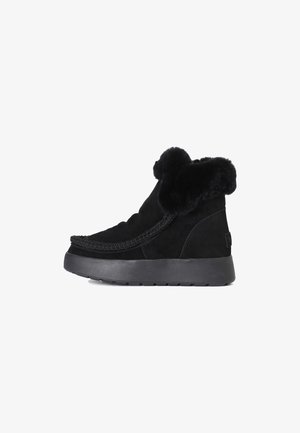 Botas de tobillo de ante negro con una suela gruesa negra, que cuentan con un puño de piel de lujo y un detalle trenzado en la parte superior. Textura suave en toda su superficie.