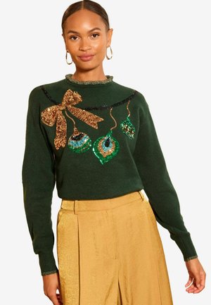 Grön tröja med rund halsringning, prydd med en guldpaljettslåt och färgglada ornamentdesigns i paljetter och pärlor. Guldbyxor.