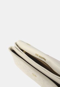 Borsa a tracolla bianca trapuntata con hardware dorato, dotata di chiusura con zip superiore e branding interno. Texture in pelle liscia con una forma strutturata.