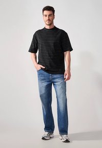 Svart kortermet t-skjorte med tynne, horisontale hvite striper, kombinert med lyseblå jeans med rette ben og sølvfargede sportssko.