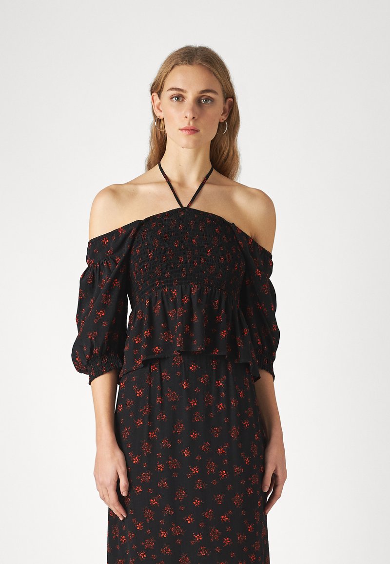 Abito nero floreale con corpetto arricciato a spalle scoperte, maniche a sbuffo e decorazioni di fiori rossi. Tessuto leggero con vestibilità rilassata.