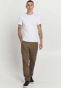 White cotton t-shirt paired with brown chinos. Black sneakers with white soles. Plain design, relaxed fit, no visible patterns or accents.