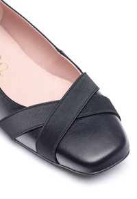 Scarpe piatte nere in pelle con punta quadrata, cinturino elastico cucito a croce e una morbida fodera interna rosa. Texture liscia e design minimalista.