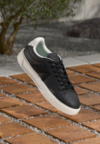 Sorte lærersneakers med hvit såle, med polstret krage, snøring og subtil merking. Teksturert gummisåle synlig.