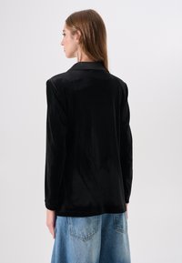 Zwart zijdenblouse met lange mouwen en een kraag, met een gladde textuur en een licht losse pasvorm, gecombineerd met lichtblauwe spijkerbroek.