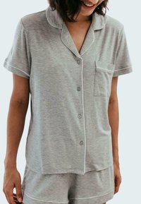 Harmaa pyjamasetti, joka on valmistettu pehmeästä kankaasta. Setissä on lyhythihainen toppi, jossa on kaulus, napit ja rintatasku, sekä siihen sopivat shortsit.