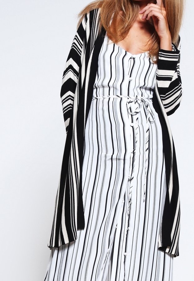 Svart och vit randig lång cardigan med öppen front och vida ärmar över en vitrandig byxdress med knappar och knytning i midjan.