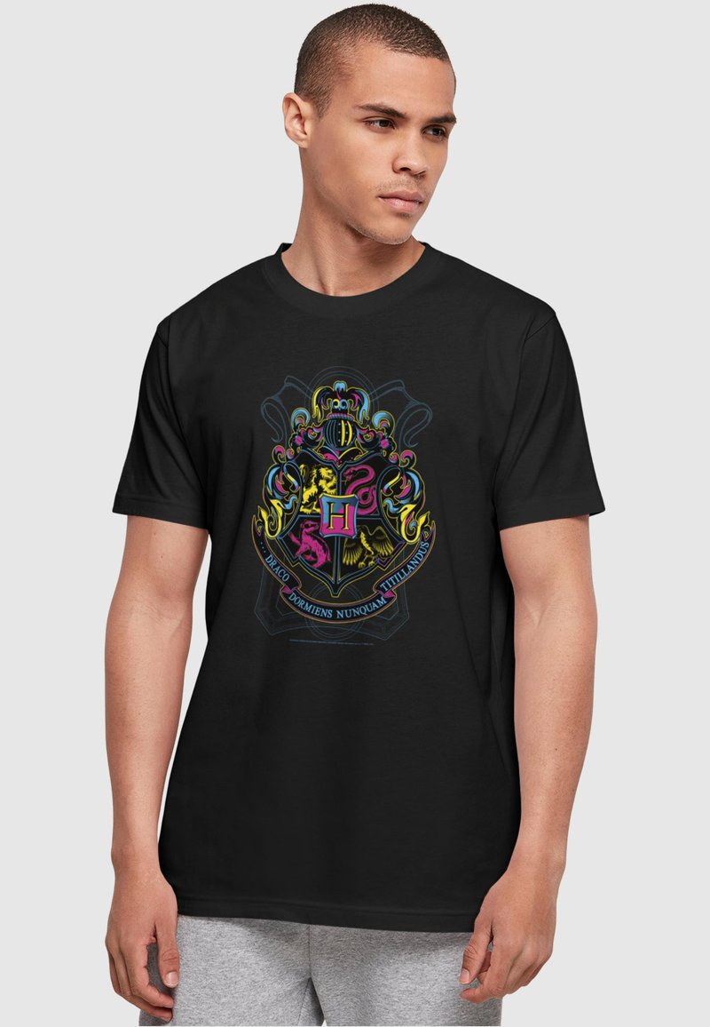 Zwarte t-shirt met een kleurrijk wapenschildontwerp met ingewikkelde details, waaronder een centrale "H," dieren en Latijnse tekst op een gladde stof.