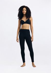 Fekete vezeték nélküli melltartó és magas derekú leggings rugalmas anyagból. A dizájn varrás nélküli, sima textúrával és testhezálló formával rendelkezik.