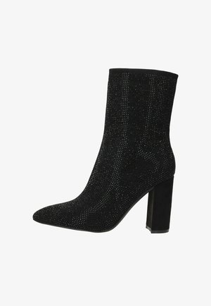 Zwarte enkellaars met een spitse neus, textiel met structuur versierd met metalen embellissementen, en een stevige hak voor ondersteuning.