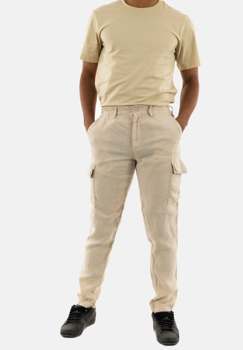 Beige cargobroek met zijzakken, knoopsluiting en een relaxte pasvorm. Gekleed met een lichtbeige T-shirt met korte mouwen en zwarte sneakers.
