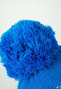 Knitted blue hat featuring a large, fluffy pom-pom on top and a textured body, made of soft yarn.