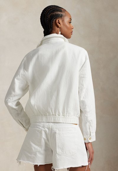 White denim jacket with a high collar and elastic waistband, paired with matching white shorts featuring frayed hems and back pockets.