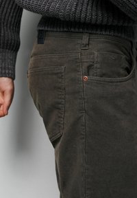 Ciemnoszare spodnie sztruksowe z teksturowaną powierzchnią, widocznymi szwami i małą kieszenią. Na tylnej części pasa znajduje się etykieta z logo marki.