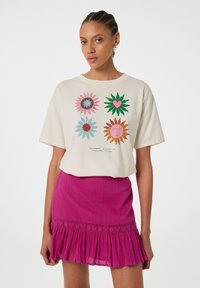 Crèmekleurig T-shirt met korte mouwen met kleurrijke bloemenprints, gecombineerd met een fuchsia geplooide rok met geborduurde zoomdetails.