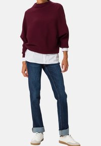 Suéter de punto oversize burdeos con cuello alto, combinado con jeans de corte estándar en azul oscuro enrollados en los puños y zapatillas blancas.