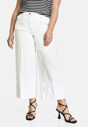 Pantalones de pierna ancha blancos con una cintura alta, confeccionados en tela de algodón. Combinados con tacones negros de tiras, que muestran un diseño minimalista.