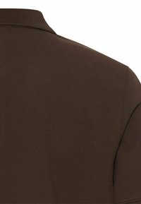 Close-up van donkerbruine stof op de schouder en kraag van een polo met korte mouwen.