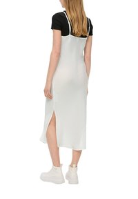 Robe nuisette blanche avec une finition texturée, dotée de bretelles spaghetti réglables et d'une fente latérale haute, portée sur une chemise noire à manches courtes.