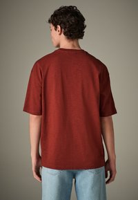 Tricou roșu cu mâneci scurte, din țesătură texturată, cu guler rotund și croială lejeră, asortat cu blugi din denim bleu deschis.