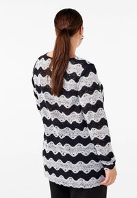 Czarny i biały sweter w faliste paski, o luźnym kroju i długich rękawach, z teksturowanym, ażurowym wzorem.