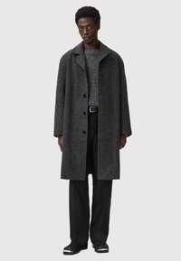 Grå uldfrakke med krave, enkeltradet design og sidelommer, parret med en grå tekstureret sweater og sorte bukser.