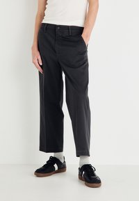 Pantalon noir à coupe régulière, en coton, avec des poches latérales. Associé à des baskets noires et des chaussettes gris clair.