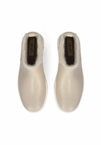 Pantofii slip-on bej au un material lucios și neted, căptușeală pufoasă bej și tălpi albe. Prezintă un eticheta de marcă subtilă la călcâi.