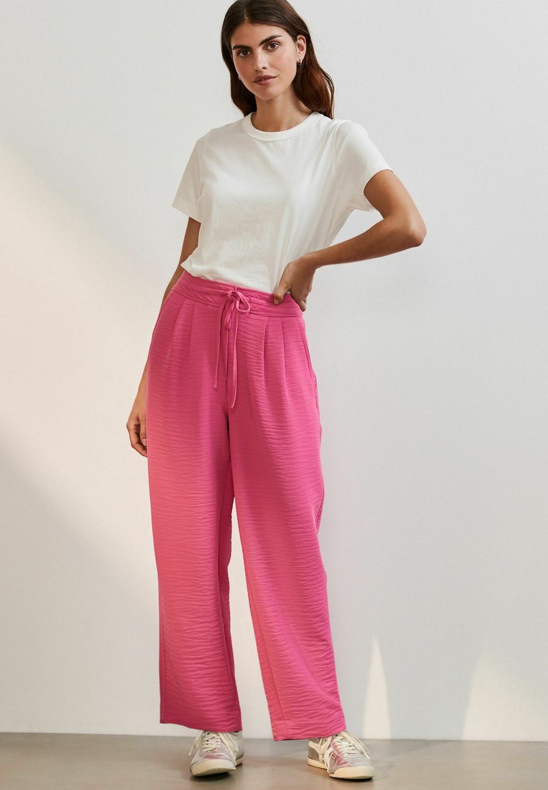 Rosa vida byxar i texturerat tyg med resårmidja, i kombination med en enkel vit T-shirt och avslappnade vita sneakers.