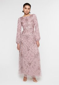 Vestido de noche rosa con cuentas, con mangas largas de tela transparente, bordados florales y una cintura ajustada. Superposición de falda transparente con un brillo sutil.