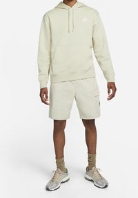 Beige hoodie med frontficka och snörning, tillsammans med matchande beige cargoshorts med sidfickor. Bärs med beige och grå sneakers.