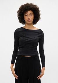 Melnas krāsas, garām piedurknēm, topiņš ar bateau dekoltē, ar tekstūrētu ziedu dizainu un rotājumiem. Pieguļošs stils, gluda auduma.