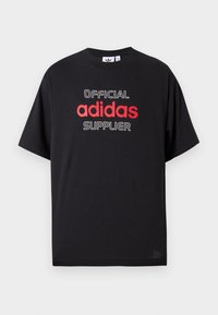 Melnas kokvilnas T-krekls ar īsām piedurknēm, ar baltu un sarkanu tekstu, kas vēsta "OFICIĀLAIS adidas PIEGĀDĀTĀJS". Klasisks apaļas kakla dizains.
