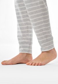 Grå och vitrandiga pyjamasbyxor i mjukt bomullstyg; med resårer vid anklarna, tillsammans med bara fötter på en vit yta.