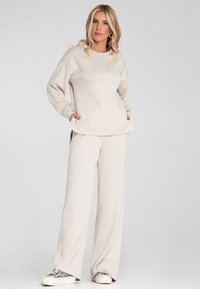 Beżowy, luźno dopasowany sweatshirt z długimi rękawami i bocznymi rozcięciami, w komplecie z dopasowanymi spodniami o szerokich nogawkach. Miękka tkanina z minimalistycznym wzorem.