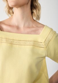 Yellow off-the-shoulder top featuring decorative lace detailing along the neckline and sleeves, made of soft cotton material.