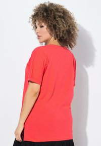 T-shirt rouge à manches courtes avec une coupe décontractée, fabriqué en tissu léger. Présente un col rond et des fentes sur les côtés à l'ourlet pour un détail supplémentaire.