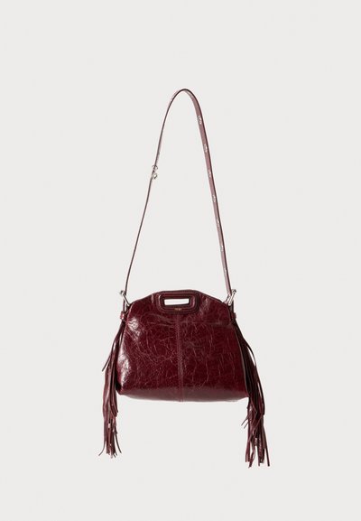 Sac à épaule en cuir rouge foncé avec longue bandoulière réglable, poignée découpée sur le dessus et pampilles à franges des deux côtés.