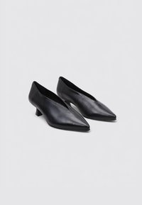 Zapatos negros de cuero con punta afilada y tacón cuadrado bajo, de diseño elegante y minimalista. Textura suave y sin herrajes o acentos visibles.