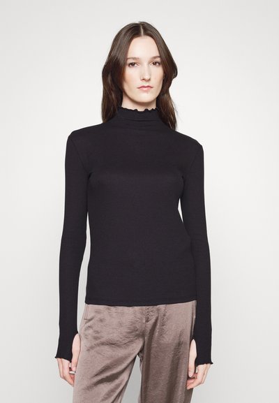 Top negro de manga larga con un cuello alto y arrugado, de textura suave, combinado con pantalones de color taupe claro que tienen un ajuste holgado y costuras laterales visibles.