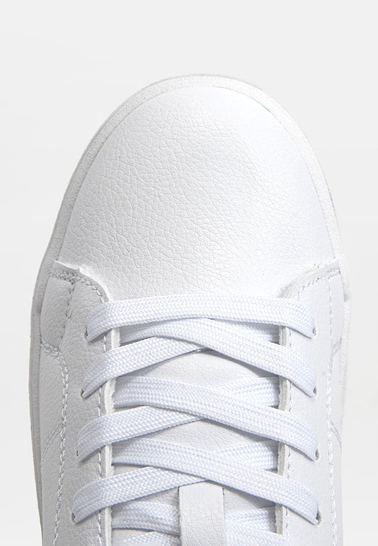 Sneaker bianco in pelle con punta rotonda, dotato di lacci piatti bianchi, superficie testurizzata e design minimalista, con dettagli di cucitura visibili.