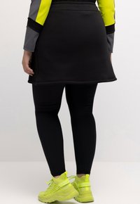 Zwarte sportrok over zwarte leggings, gecombineerd met fel neon groene sneakers met mesh en veters voor een veilige pasvorm.