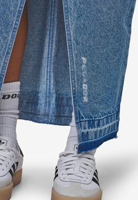 Jeanskjørt med rå kant og lysere blå vask, med en sidehakk. Kombinert med hvite joggesko og hvite, merkede sokker.