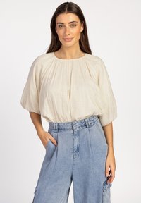 Lichtbeige, gestructureerde blouse met een ronde halslijn en geplooide details, gecombineerd met hoge taille, lichtblauwe denim broeken.