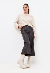Pulover tricotat bej, pantaloni largi din piele neagră cu talie înaltă și fermoar lateral, și cizme de luptă crem cu șireturi și tălpi texturate.